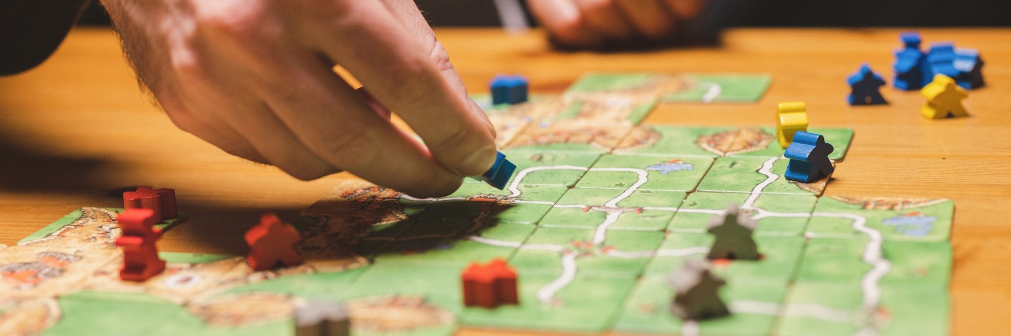 men friends have fun playing the carcassonne board game at night. male hands and game cards and chip